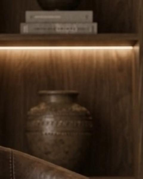 Walnut shelving lit from within, holding a textured clay jar